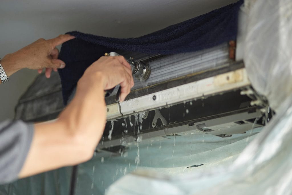 A man doing maintenance on an AC unit testing the leakage with a hose