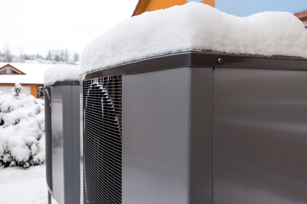 A heat pump with snow build up on top showcasing a way to save money